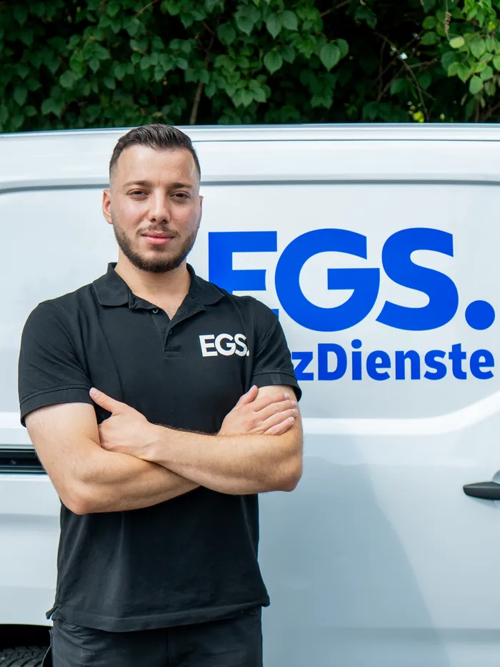 EGS-Monteur in Arbeitskleidung, mit verschränkten Armen vor seinem weißen Firmenfahrzeug mit EGS-Logo